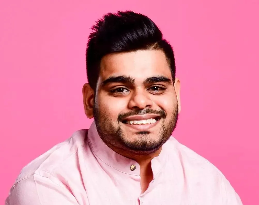 A smiling man in a pink shirt against a pink background
